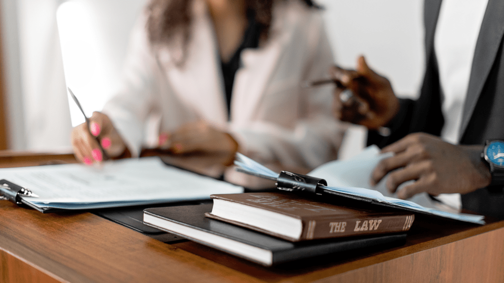 A person signing a contract in front of a table with a scale of justice