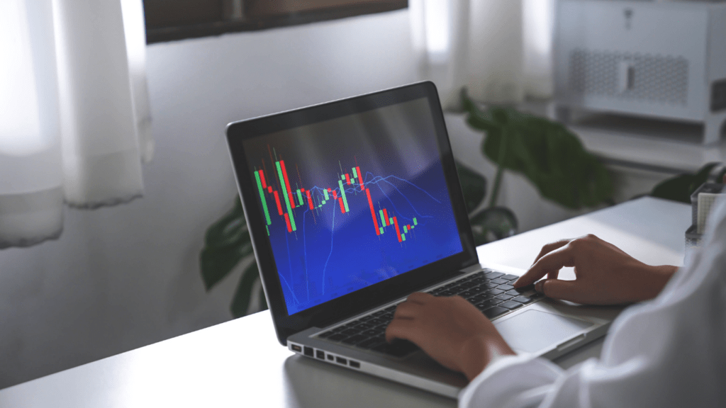 A person working on a laptop in front of a stock market screen