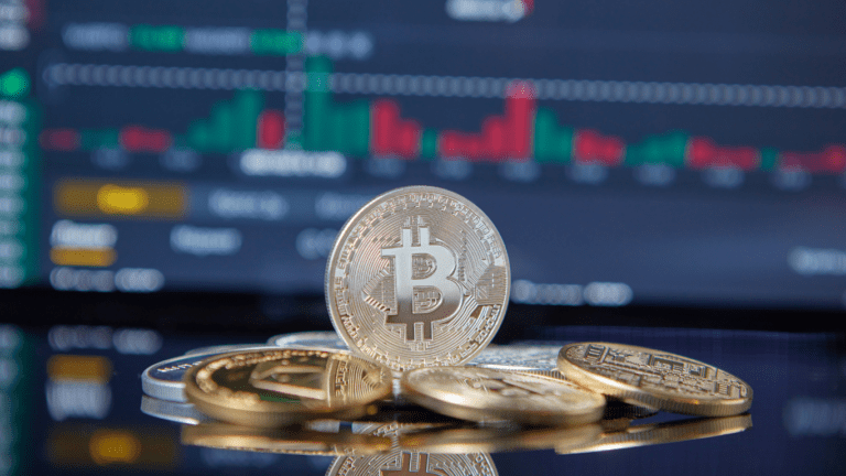 bitcoin and gold coins on a table with a stock market screen in the background