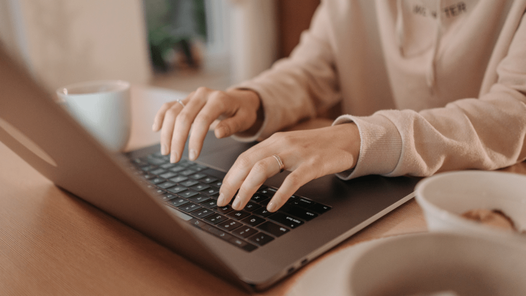 a person typing on a laptop computer with a cup of coffee in front of them