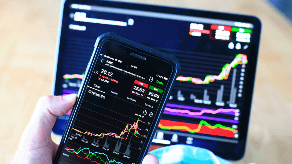 a person holding a smart phone in front of a stock market graph