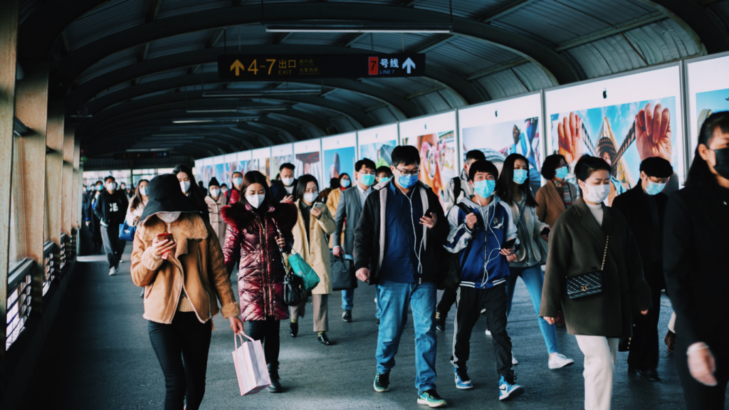 people wearing face masks walk through a subway station