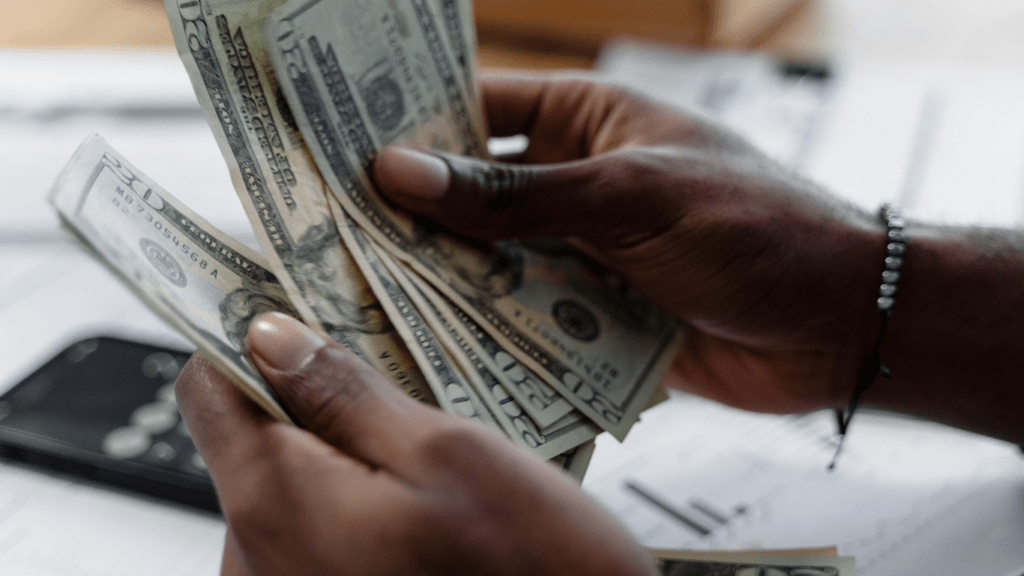 a person holding a stack of cash in front of a desk