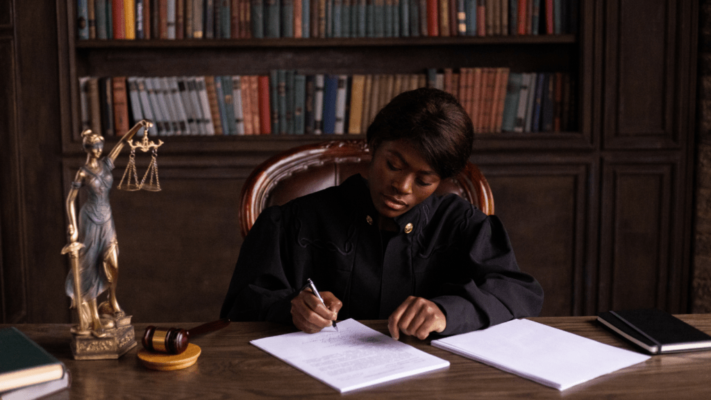 a person in a suit sitting at a desk with a scale of justice