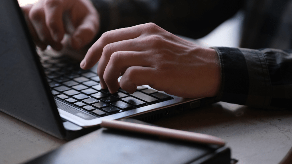 a person typing on a laptop computer with a cup of coffee in front of them